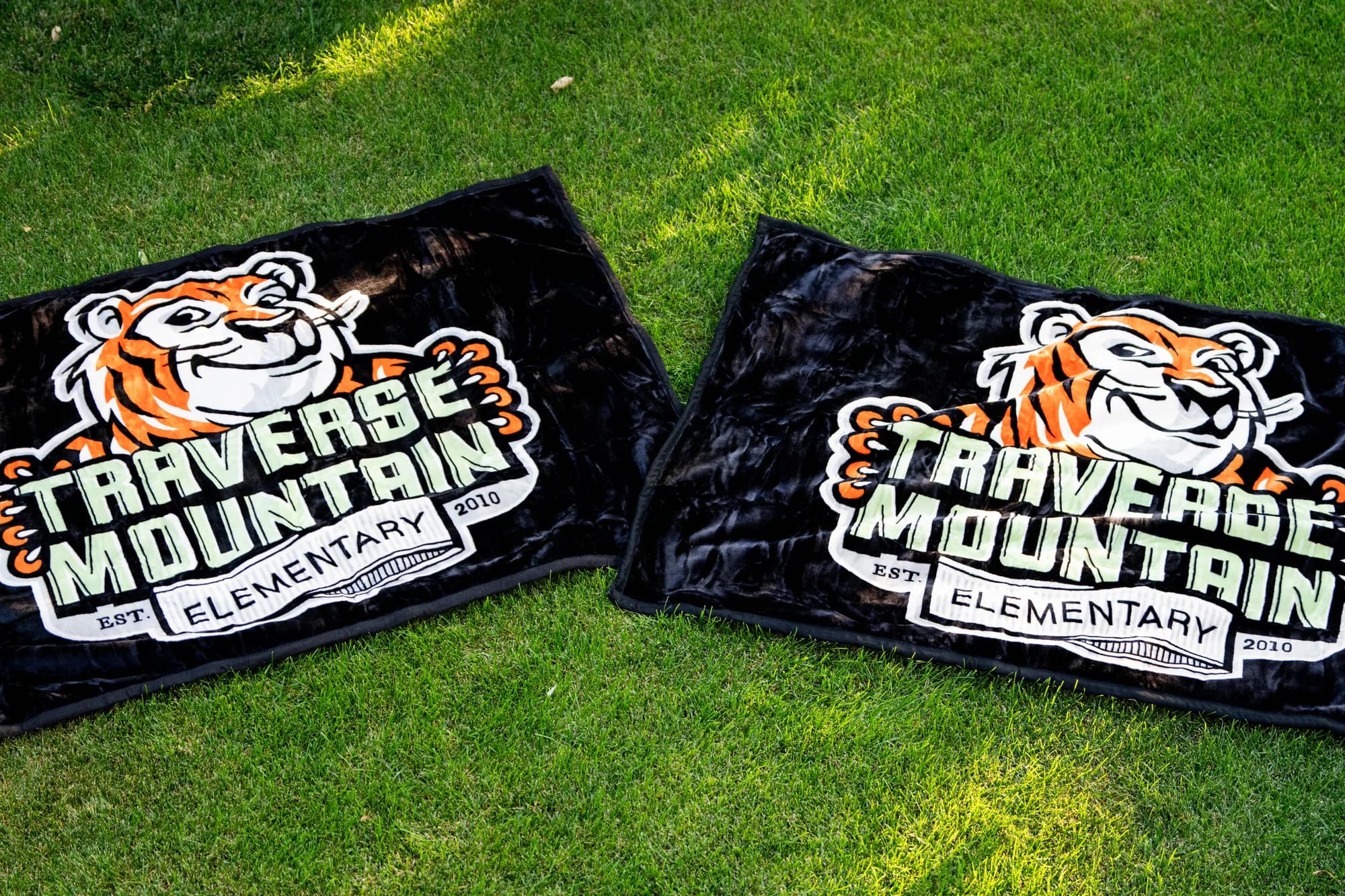 Two custom printed Traverse Mountain Elementary tiger blankets laid out on the grass