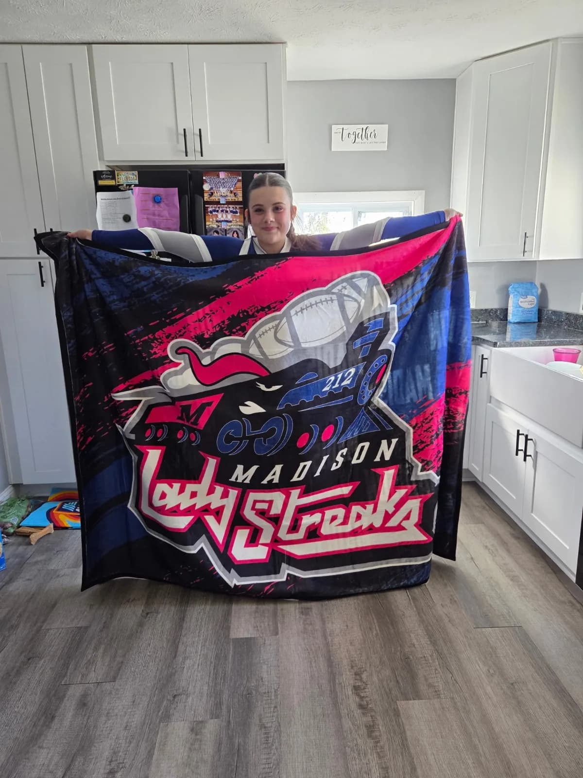 A real customer holding up her custom printed Madison Lady Streaks blanket in her kitchen
